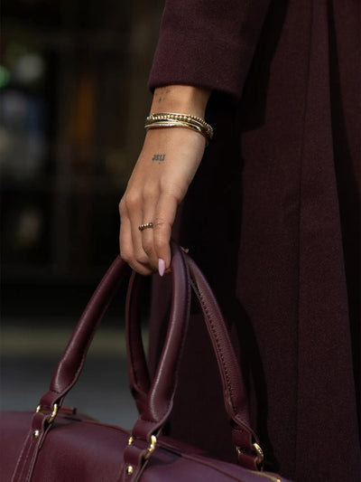 Een bordeauxrode leren handtas met goudkleurige hardware en gestructureerde handvatten.