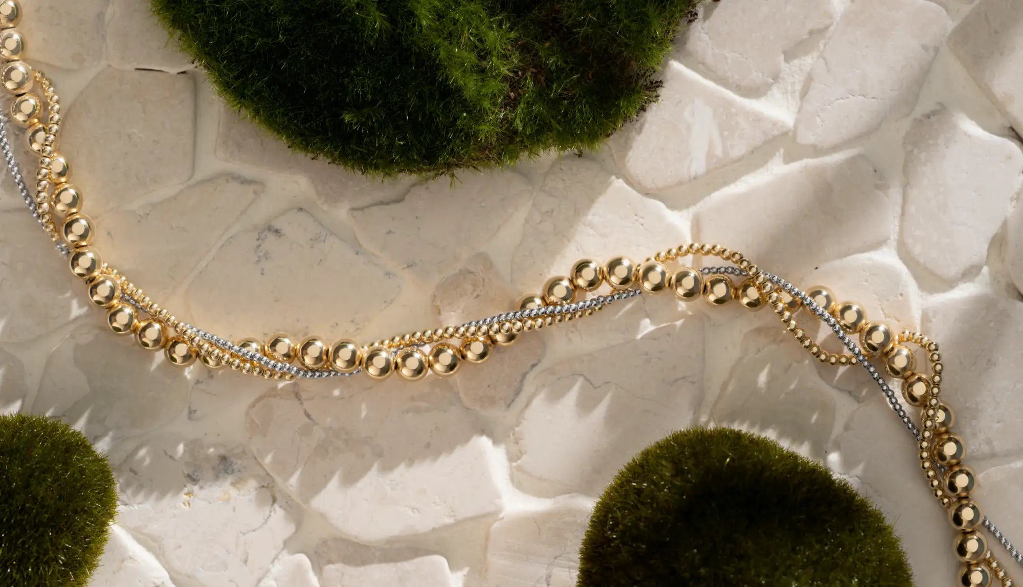 Een delicate tweedelige kralenketting met afwisselend gouden en zilveren bolvormige kralen, elegant gerangschikt in een vloeiend patroon.
