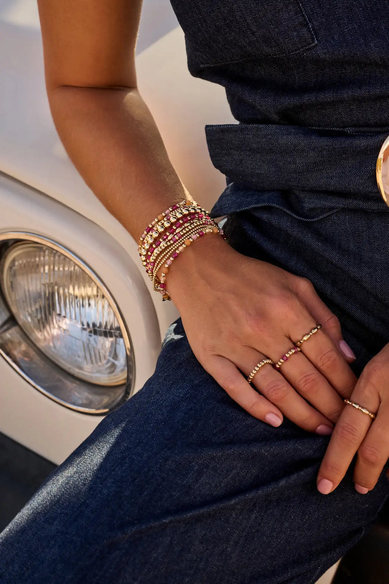 Gestapelde armbanden in goudtint, versierd met rode en heldere edelstenen, gedragen om een pols.