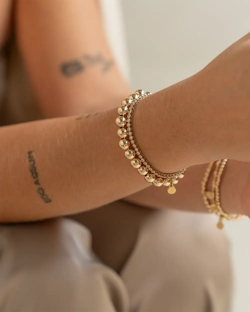 Goudkleurige kralenarmband met een delicate ketting en klein bungelend hangertje.