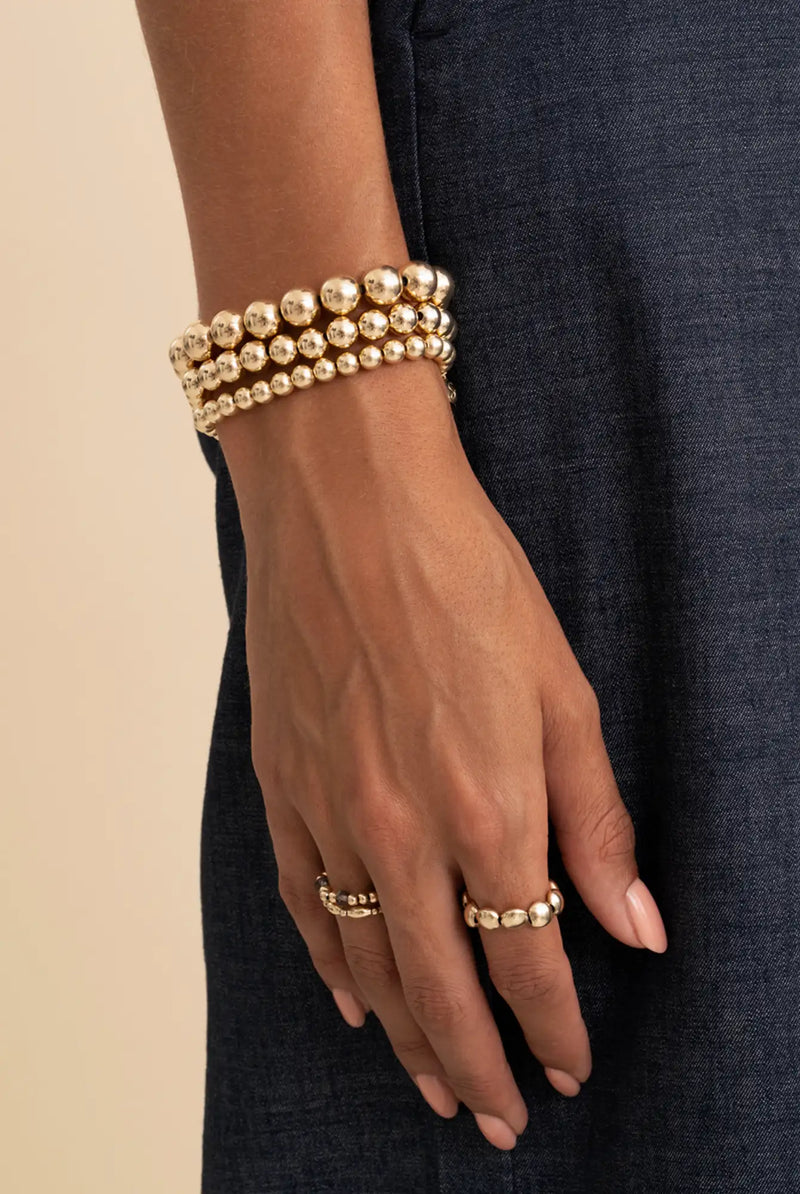 Goudkleurige kralenarmband met drie gestapelde rijen van uniform grote, gepolijste bolvormige kralen.