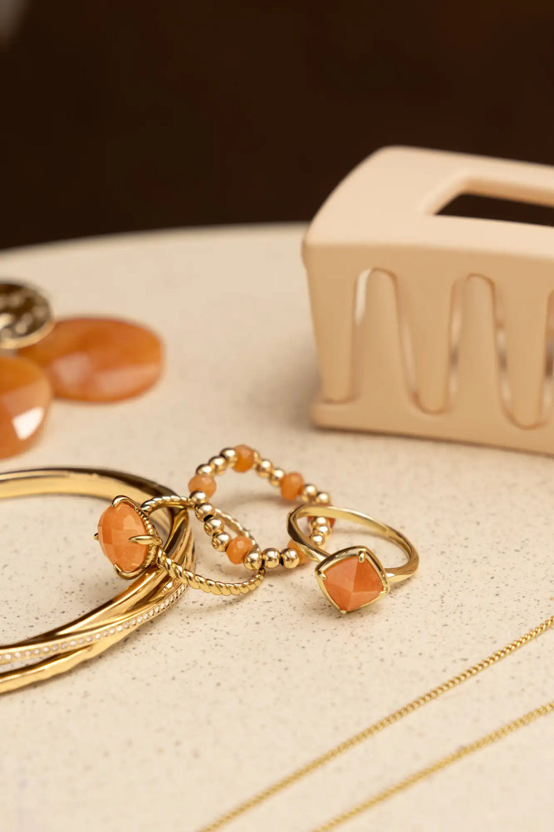 Goudkleurige ringen met gefacetteerde oranje edelstenen en delicate kraaldetails.