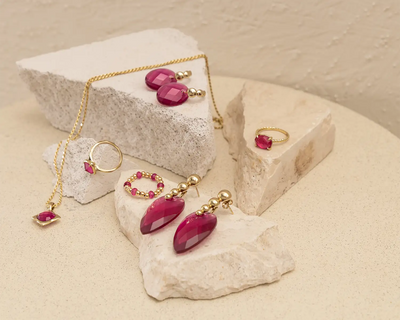 Een paar elegante, gefacetteerde fuchsia edelsteen oorbellen met goudkleurige metalen zettingen en kleine bolvormige accenten.